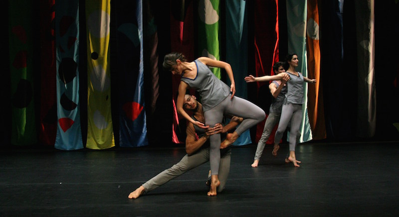 Compagnie CNDC-Angers dancers take various poses in grey leggings and tank tops with vibrant taprestries hanging in the background